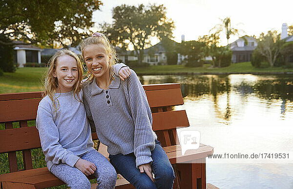 Smiling girls sitting on bench by pond