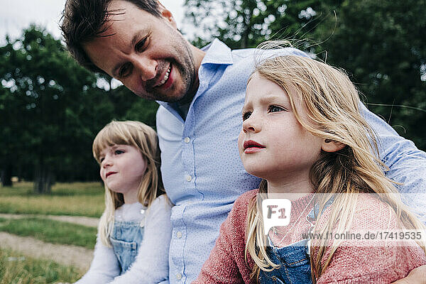 Lächelnder Vater blickt Tochter an  während er im Park sitzt