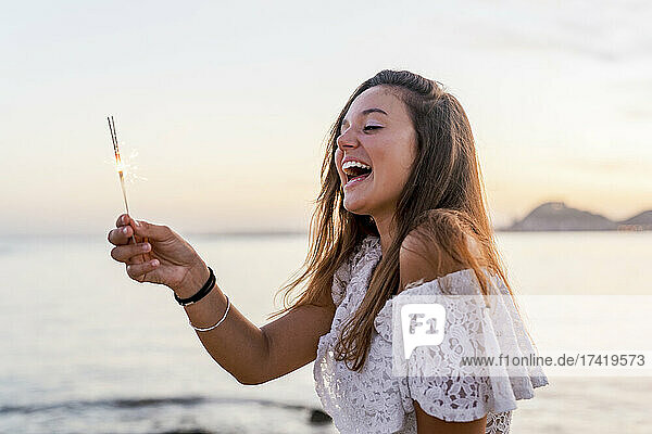 Fröhliche junge Frau hält Wunderkerze am Strand