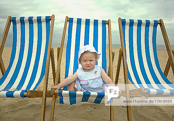 Cute baby girl sitting on deck chair at beach