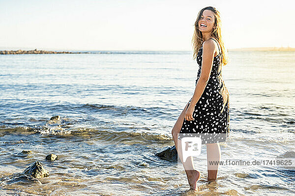 Happy young woman standing in water at seashore