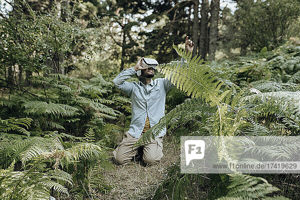 Man using virtual reality headset while kneeling in forest