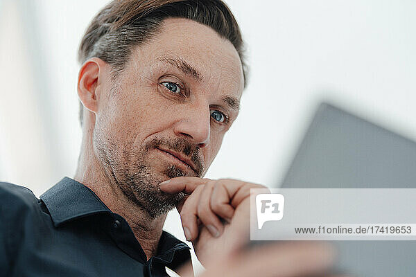 Businessman with hand on chin looking at digital tablet in office