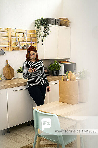 Redhead woman using mobile phone while standing in kitchen