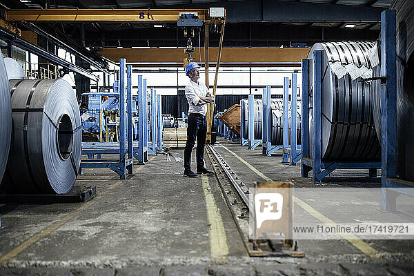 Male engineer standing with arms crossed in steel warehouse