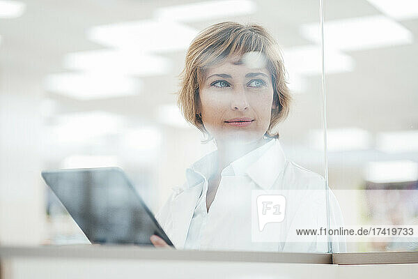 Female chemist with digital tablet looking through glass window