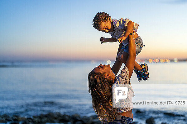 Fröhliche Mutter hebt Sohn am Strand hoch
