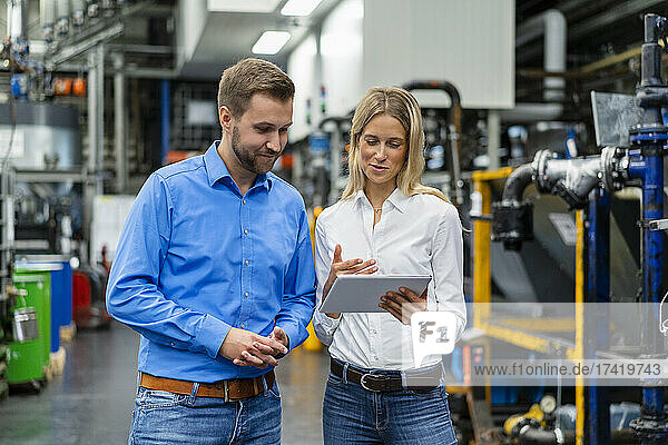 Female professional explaining colleague over digital tablet in factory