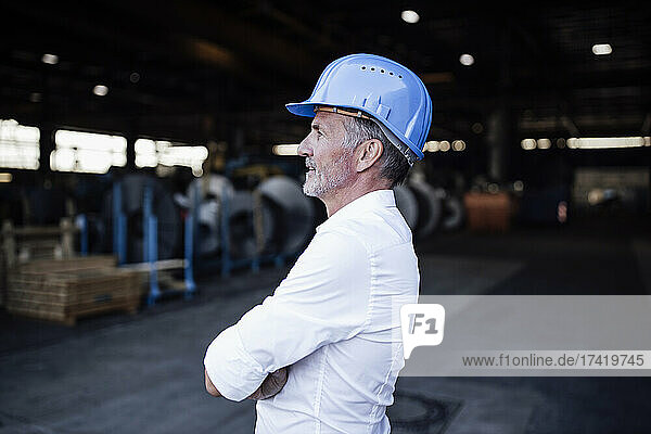 Male engineer wearing hardhat standing with arms crossed at metal industry