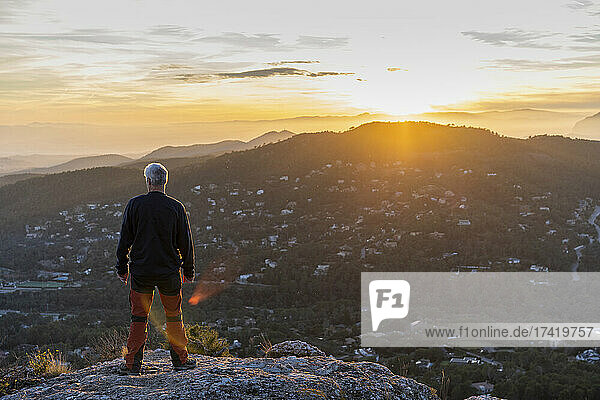 Man looking at mountain while standing at cliff during sunset