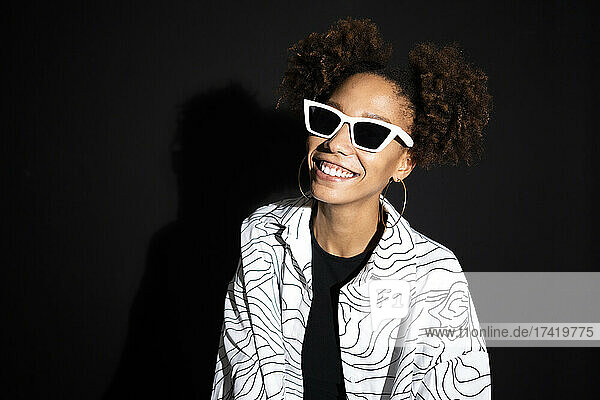 Happy fashionable woman wearing white sunglasses against black background