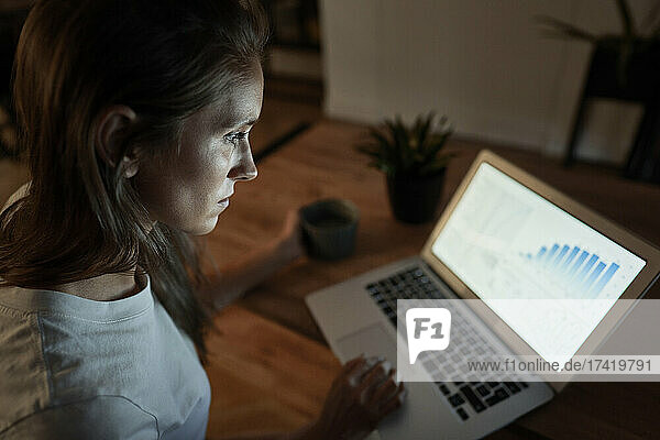 Geschäftsfrau schaut nachts zu Hause auf das Diagramm auf dem Laptop
