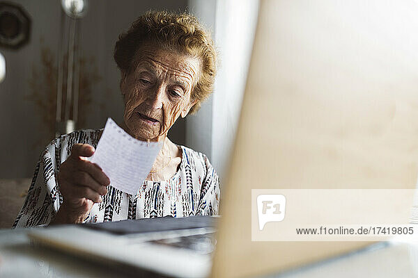 Senior woman reading letter while sitting with laptop at home
