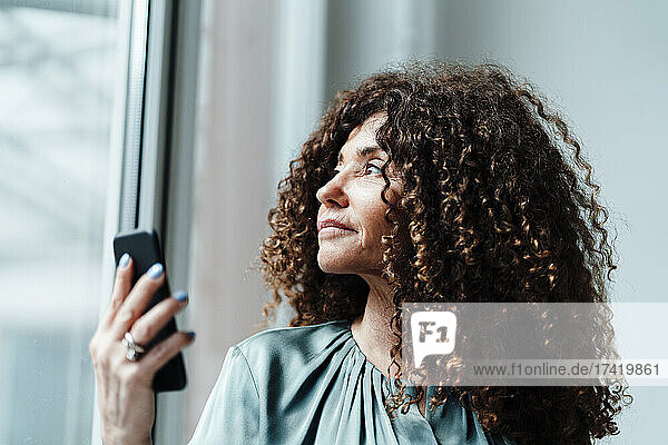 Businesswoman looking through glass while holding smart phone