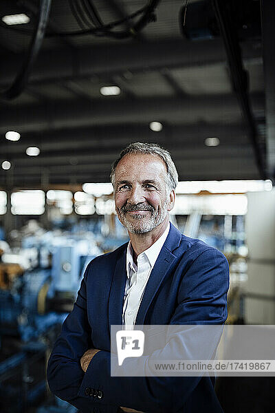 Smiling senior businessman with arms crossed at metal industry