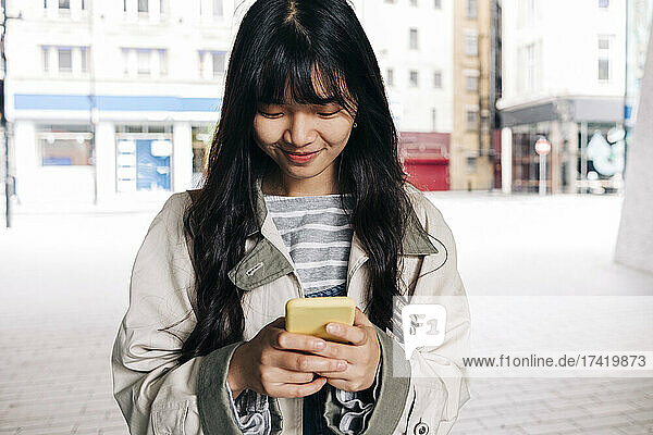 Smiling woman text messaging through smart phone in city