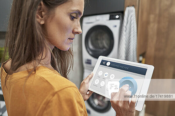 Frau nutzt digitales Tablet  um Waschmaschine zu Hause zu bedienen