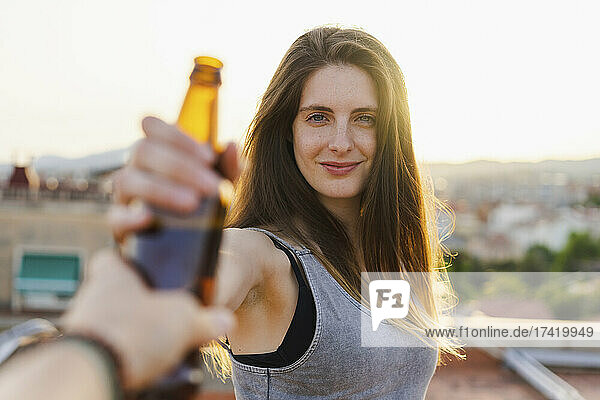 Smiling woman taking beer bottle from friend at rooftop