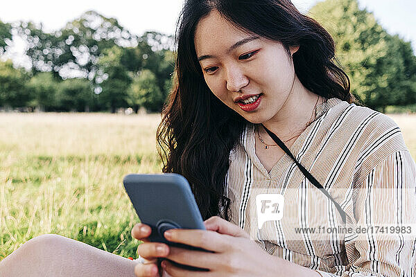 Junge Frau benutzt Smartphone  während sie auf der Wiese sitzt