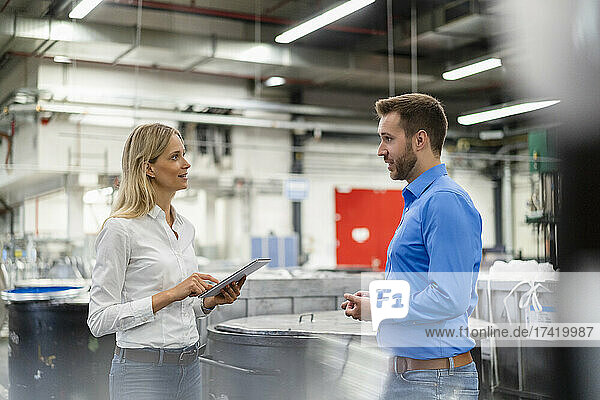 Young businesswoman holding digital tablet while discussing with colleague in factory