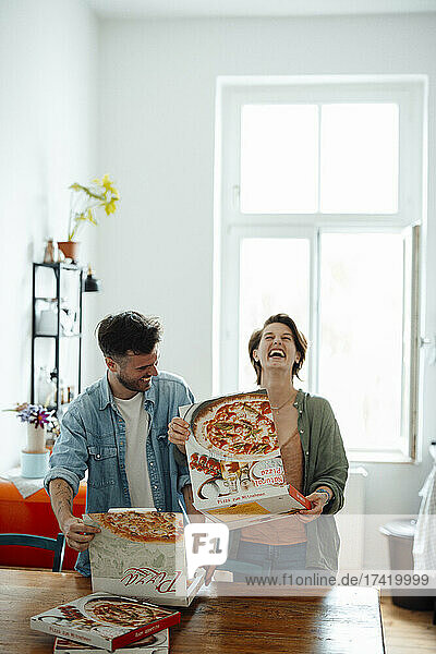 Happy couple opening pizza boxes at home