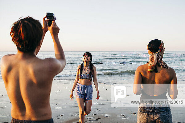 Young man photographing female friend at beach
