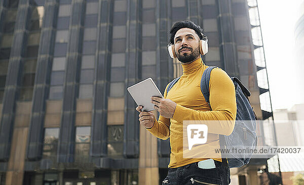 Handsome man listening music holding digital tablet in city