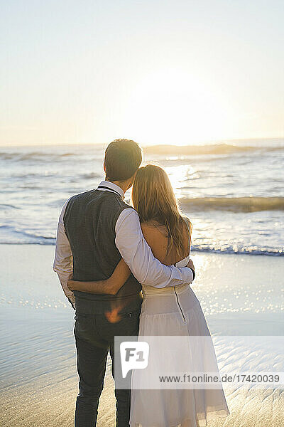 Newlywed couple with arm around at beach