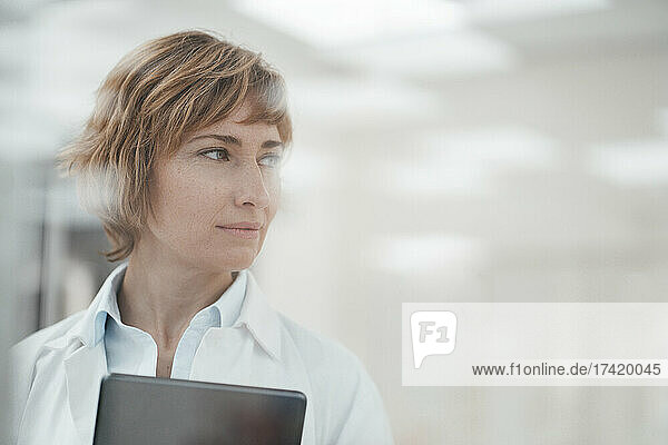 Mature female expertise with digital tablet looking away at pharmacy store