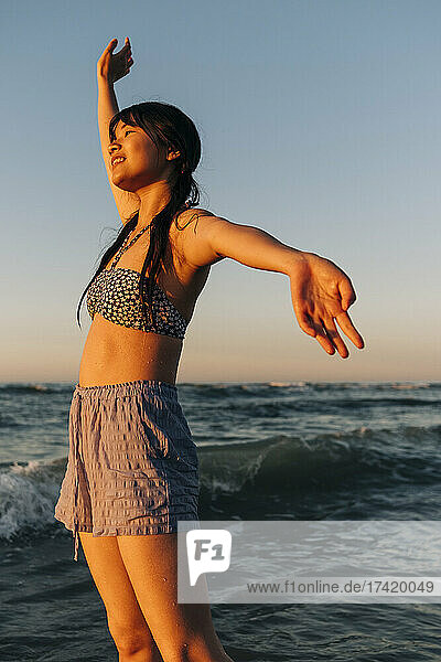 Carefree young woman with arms outstretched standing at beach