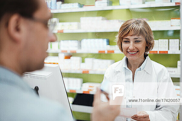 Smiling female pharmacist looking at customer checking medicine