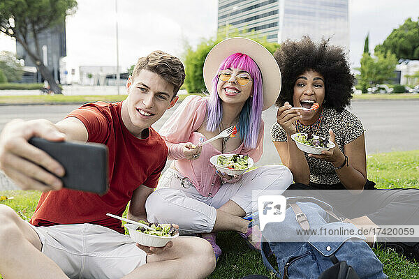 Man taking selfie with female friends holding salad at park