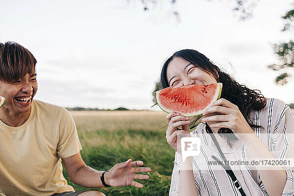 Cheerful woman having watermelon with friend at park