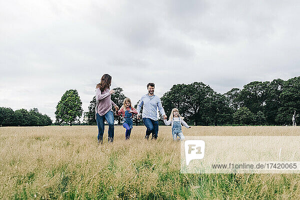Parents holding hands of daughters while running on meadow