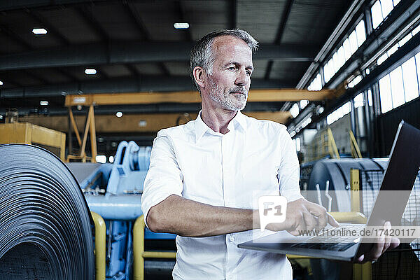Businessman using laptop while standing at metal industry