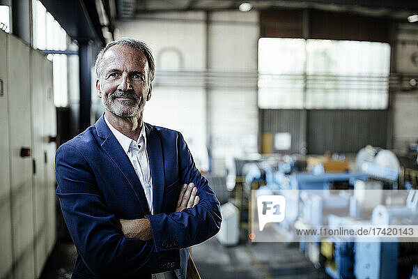 Male business professional with arms crossed standing at metal industry