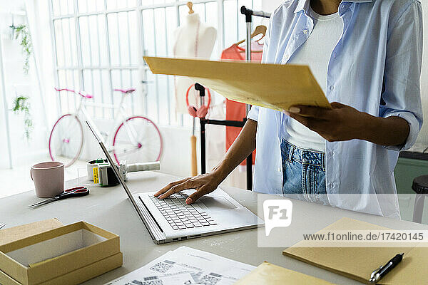 Female entrepreneur holding envelope while using laptop in studio