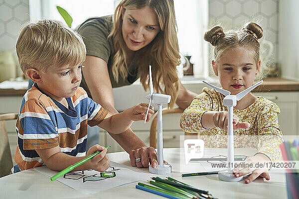 Mother teaching about wind turbine model to children at home