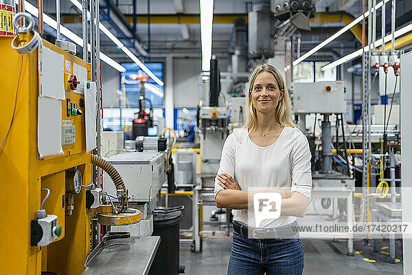 Female professional with arms crossed standing by machinery in factory