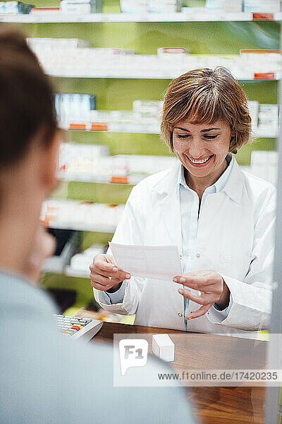 Lächelnder Apotheker liest das Rezept  während er mit dem Kunden im Geschäft steht