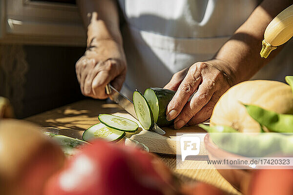 Senior woman cutting cucumber in kitchen