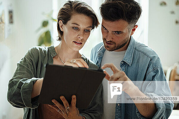 Male and female colleague discussing over graphic tablet while working at home