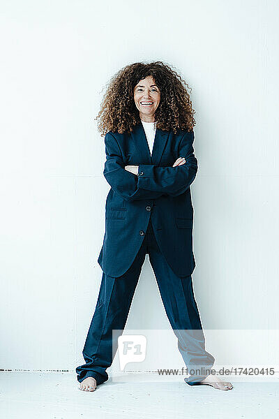 Female professional with arms crossed wearing oversized suit in front of wall