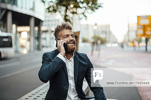 Happy male professional talking through smart phone on bench