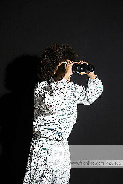 Young woman looking through binocular against black background