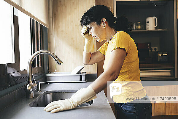Tired woman standing by utensils at kitchen sink at home