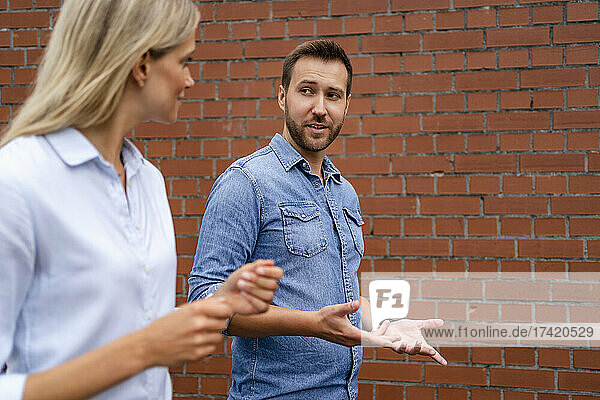 Businessman having discussion with colleague while standing by wall