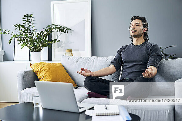 Male professional meditating while sitting on sofa at home