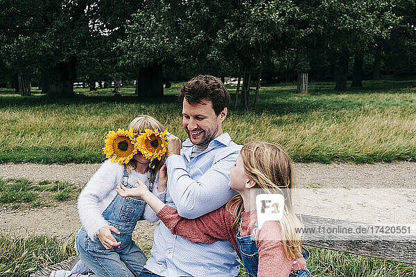 Father covering face of girl with sunflowers while playing at park