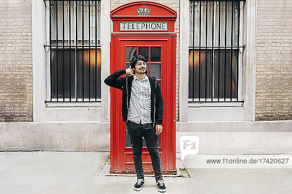 Man gesturing call me while standing in front of telephone booth